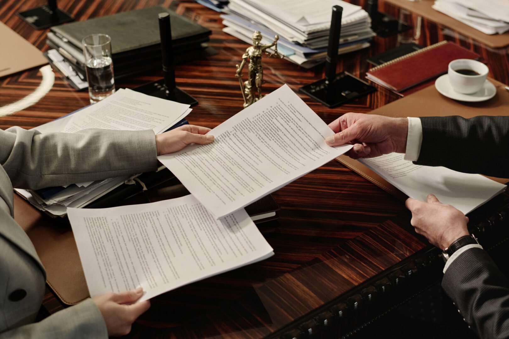 Two people exchanging documents over a wooden table.